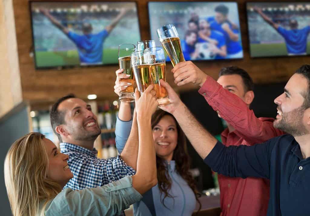 Group of Latin American friends watching a football game and making a toast at a sports bar