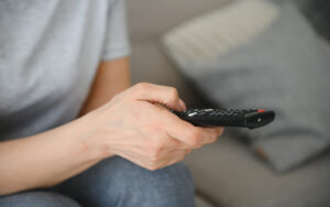 Side view of a person holding a remote control while pointing it at the TV