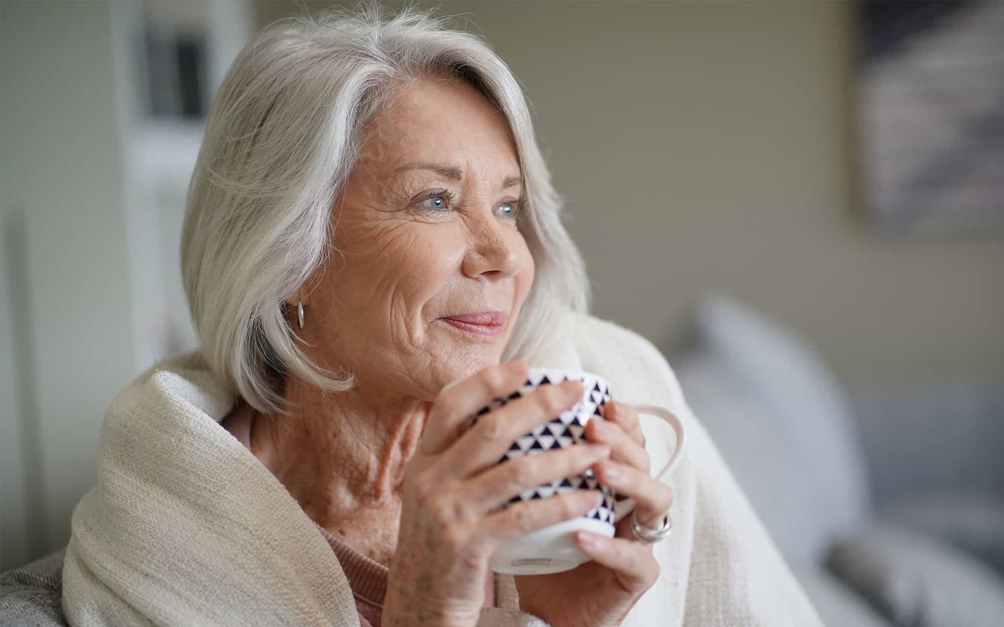 Cosy looking senior woman at home with hot drink