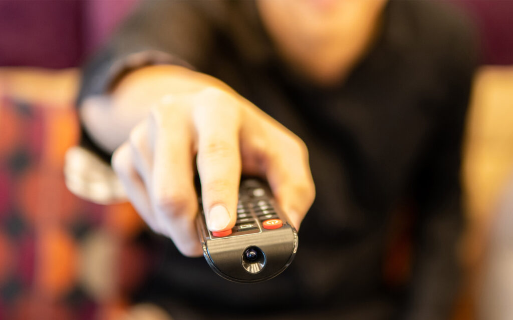 Close up of male hand using remote controller while watching TV on sofa in home