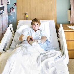 A female hospital patient uses the television remote control while lying in bed.